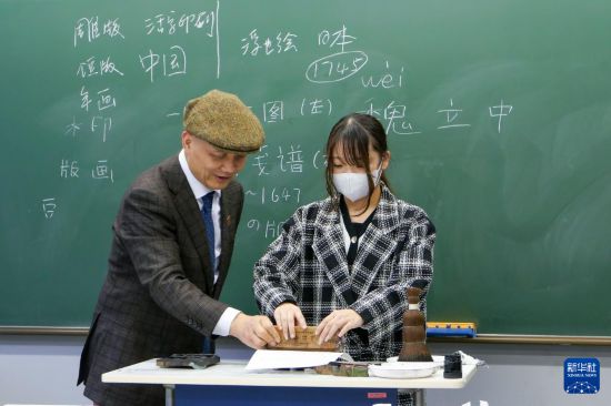 12月19日，在日本東京都的中央大學，木版水印傳承人、浙江十竹齋版畫博物館館長魏立中（左）指導(dǎo)一名大學生體驗?zāi)景嫠〖妓?。新華社發(fā)